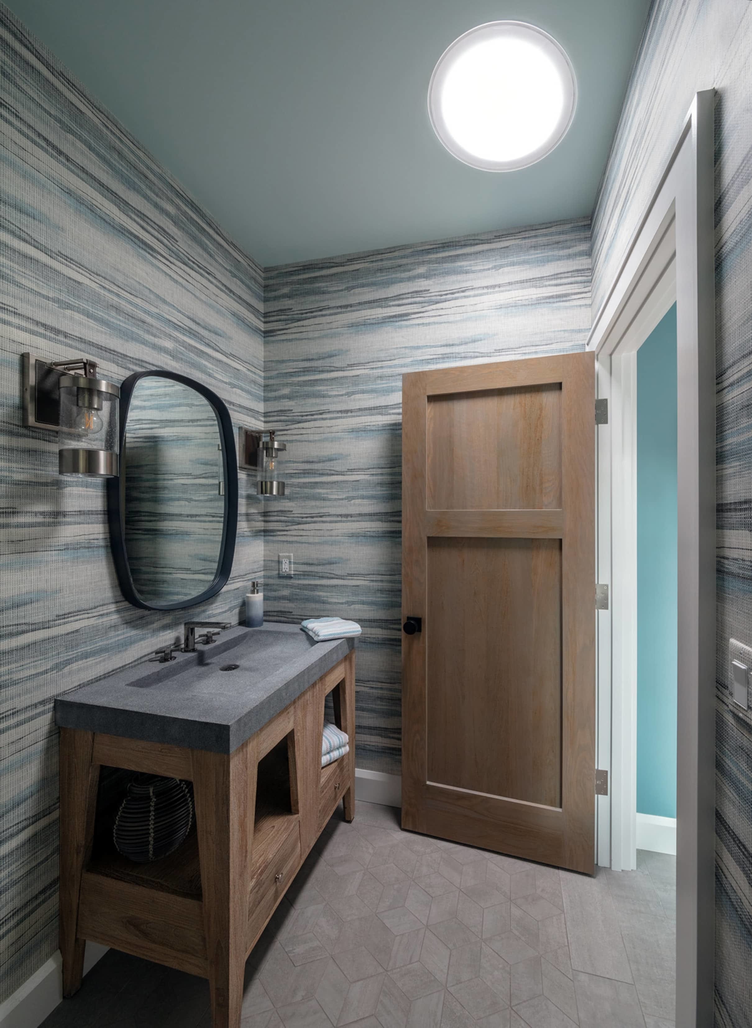bathroom with subtle wallpaper and wood and stone features with a Sun Tunnel over the vanity