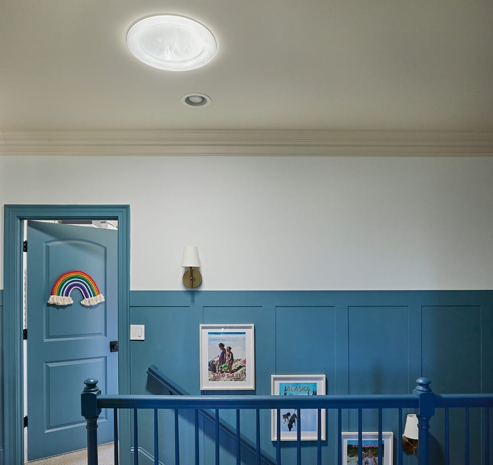 A VELUX Sun Tunnel skylight brightens the top of a stairwell leading to a hallway with wainscoting painted blue.