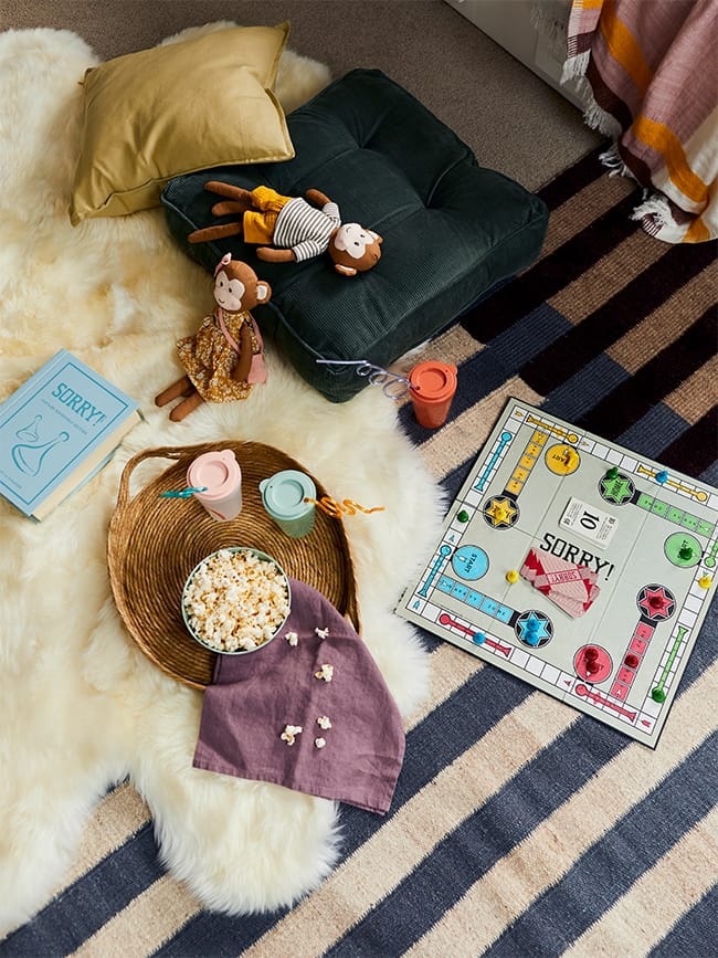 A blue and white striped rug with a wool rug layered over it with games and snacks