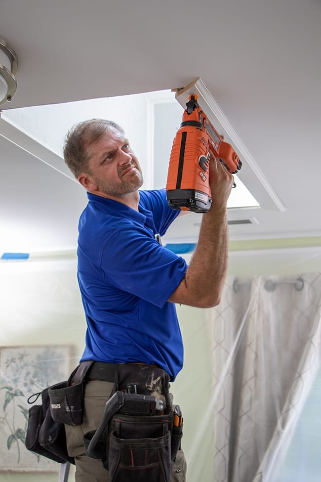 A skylight installer nails a trim piece to the light shaft opening