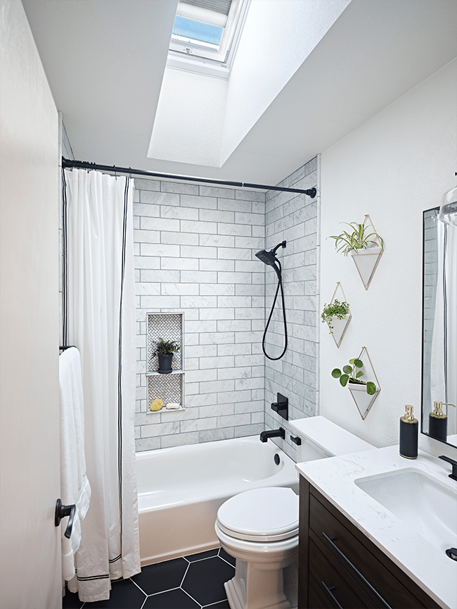 A small bathroom with a skylight white walls and black hexagonal floor tiles