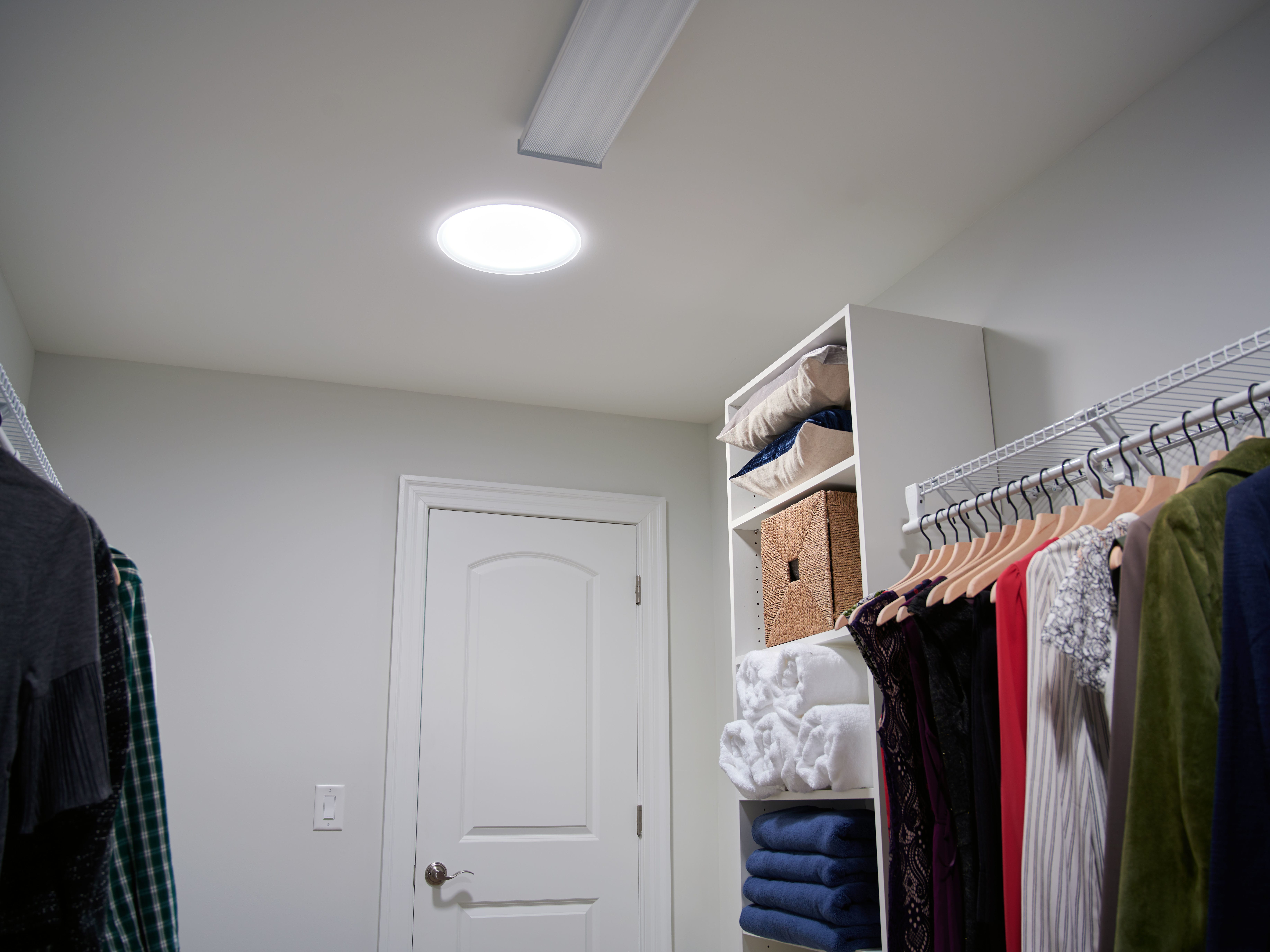 Closet with a Sun Tunnel skylight clothes on hangers and towels on a shelf