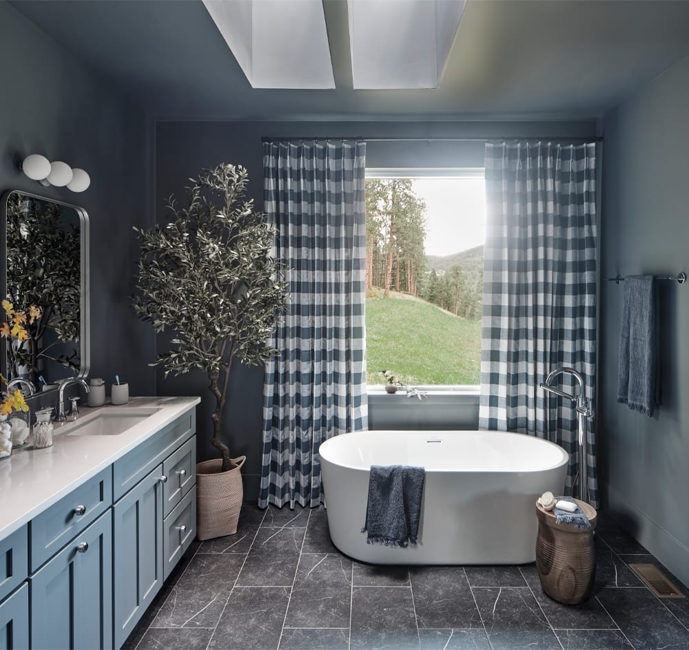 A dark gray bathroom with skylights soaking tub and light blue vanity