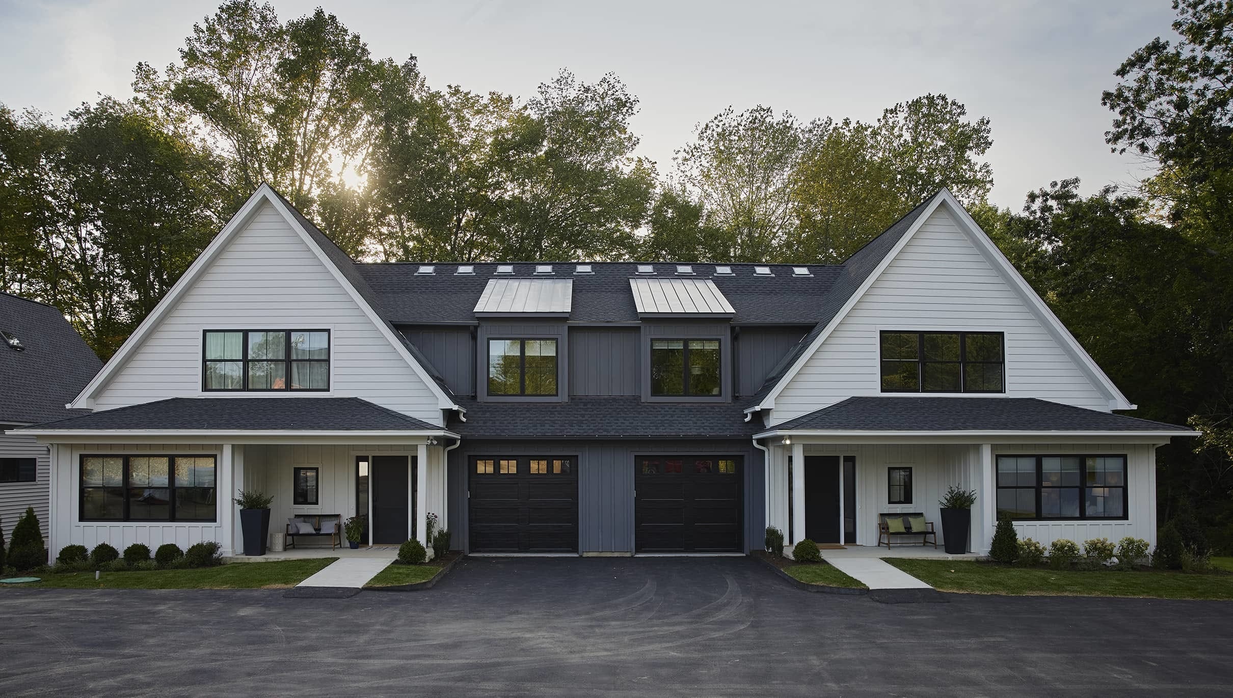 Duplex home with white siding, black trim trees in the background and setting sun