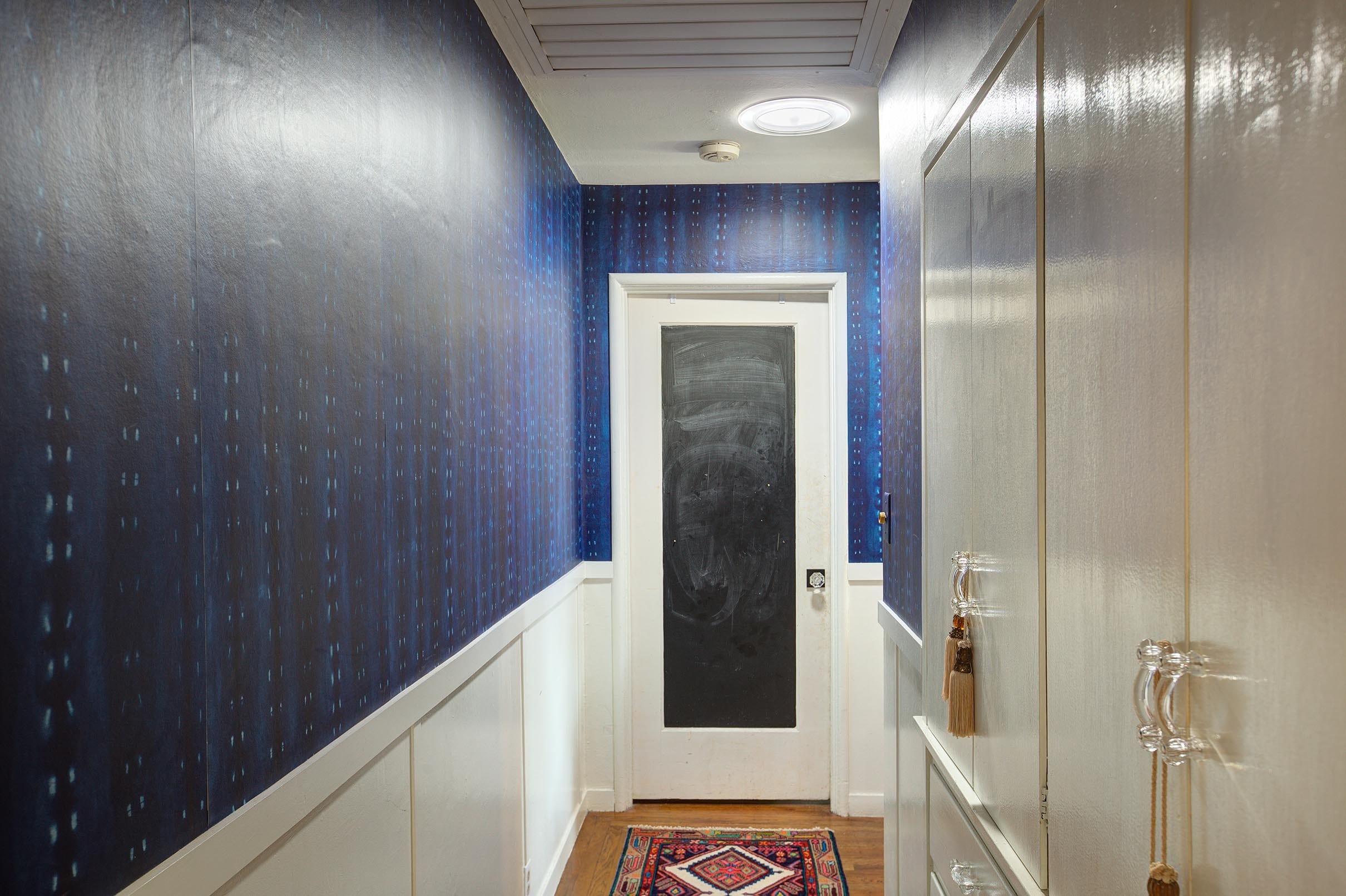 A Sun Tunnel skylight brightens a hallway with dark blue wallpaper and a vintage runner rug.