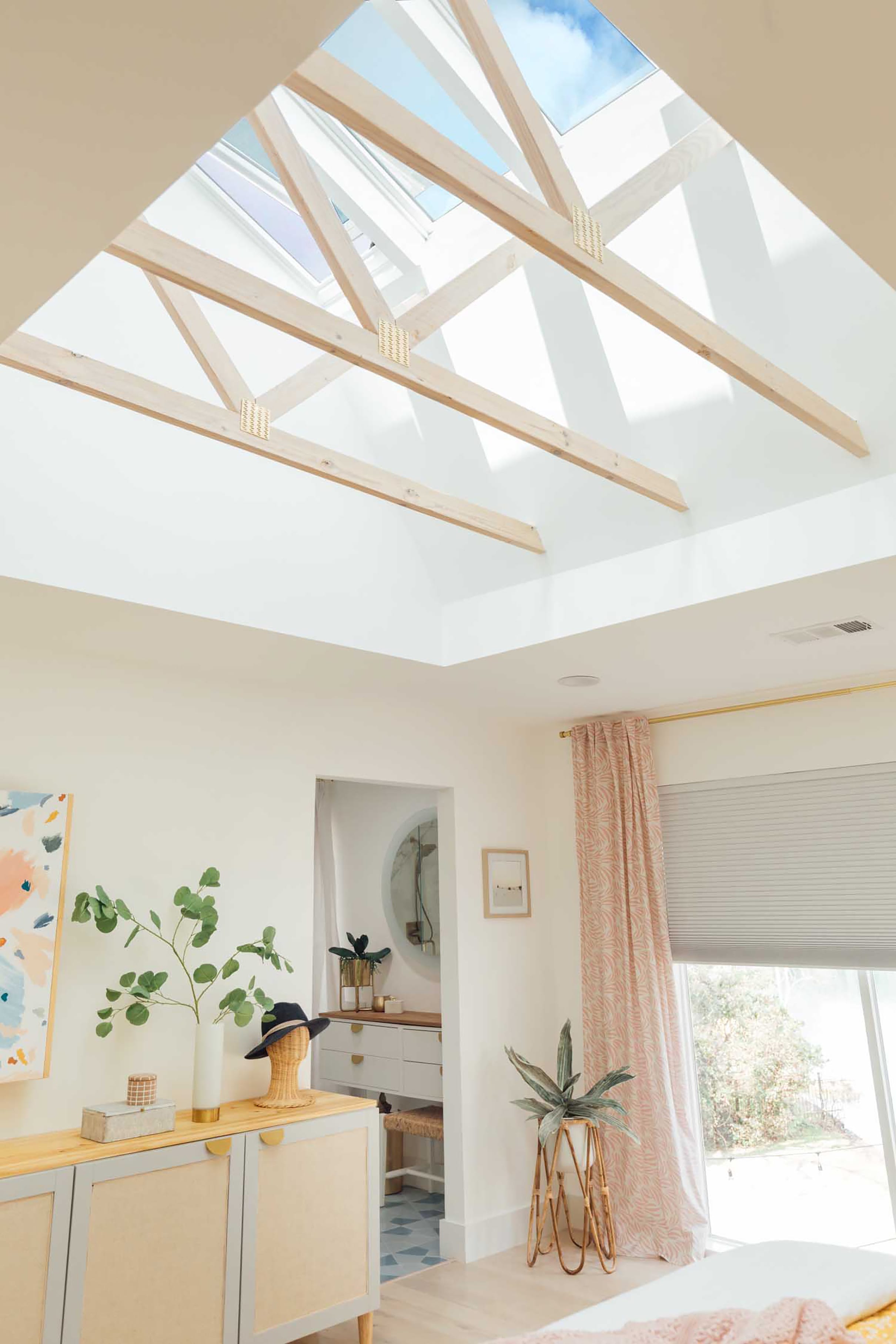 Bedroom with pink and yellow color accents and three skylights with exposed trusses.