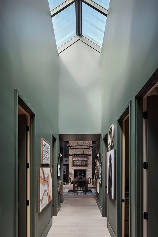 Skylights line a tall hallway painted green with a gallery wall on both sides