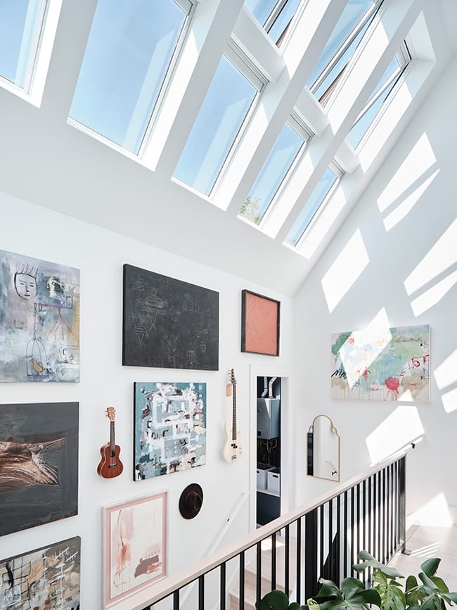Sunlight through skylights brightens a stairwell with a gallery wall