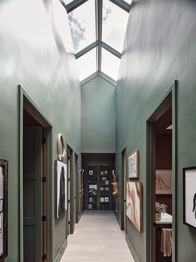 Tall hallway topped with skylights that brighten its green walls and artwork