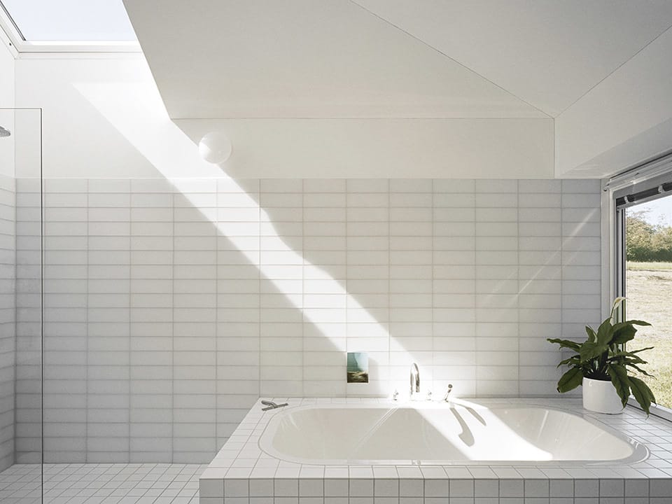 White tile bathroom with a skylight that has sun shining through it.