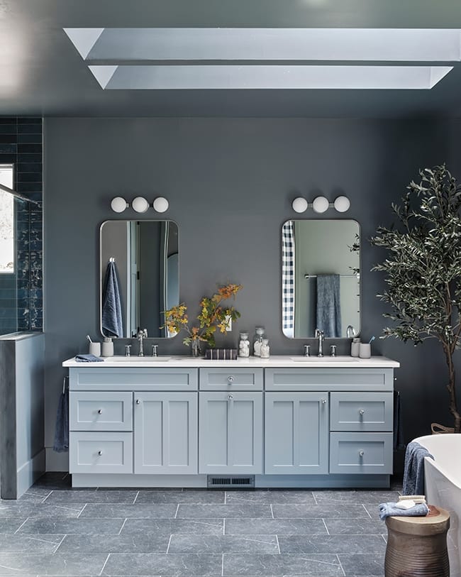 Bathroom with dark dray walls gray tile flooring a light blue vanity and three skylights