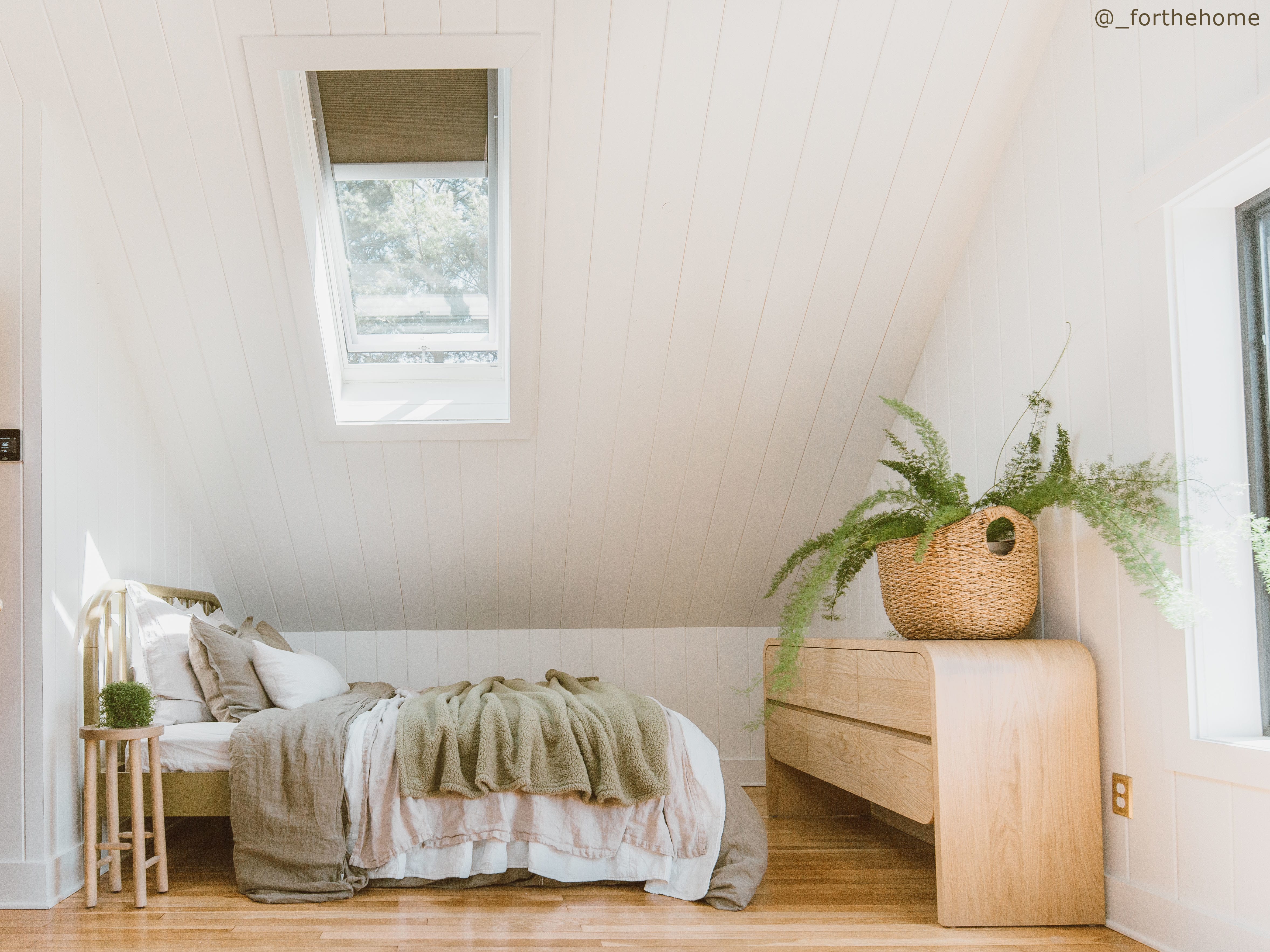 Bedroom with blond wood floors white shiplap walls and a skylight with room darkening blinds.
