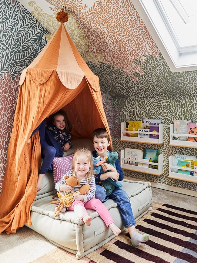 Children sitting on a cushion under an orange canopy that serves as a book nook