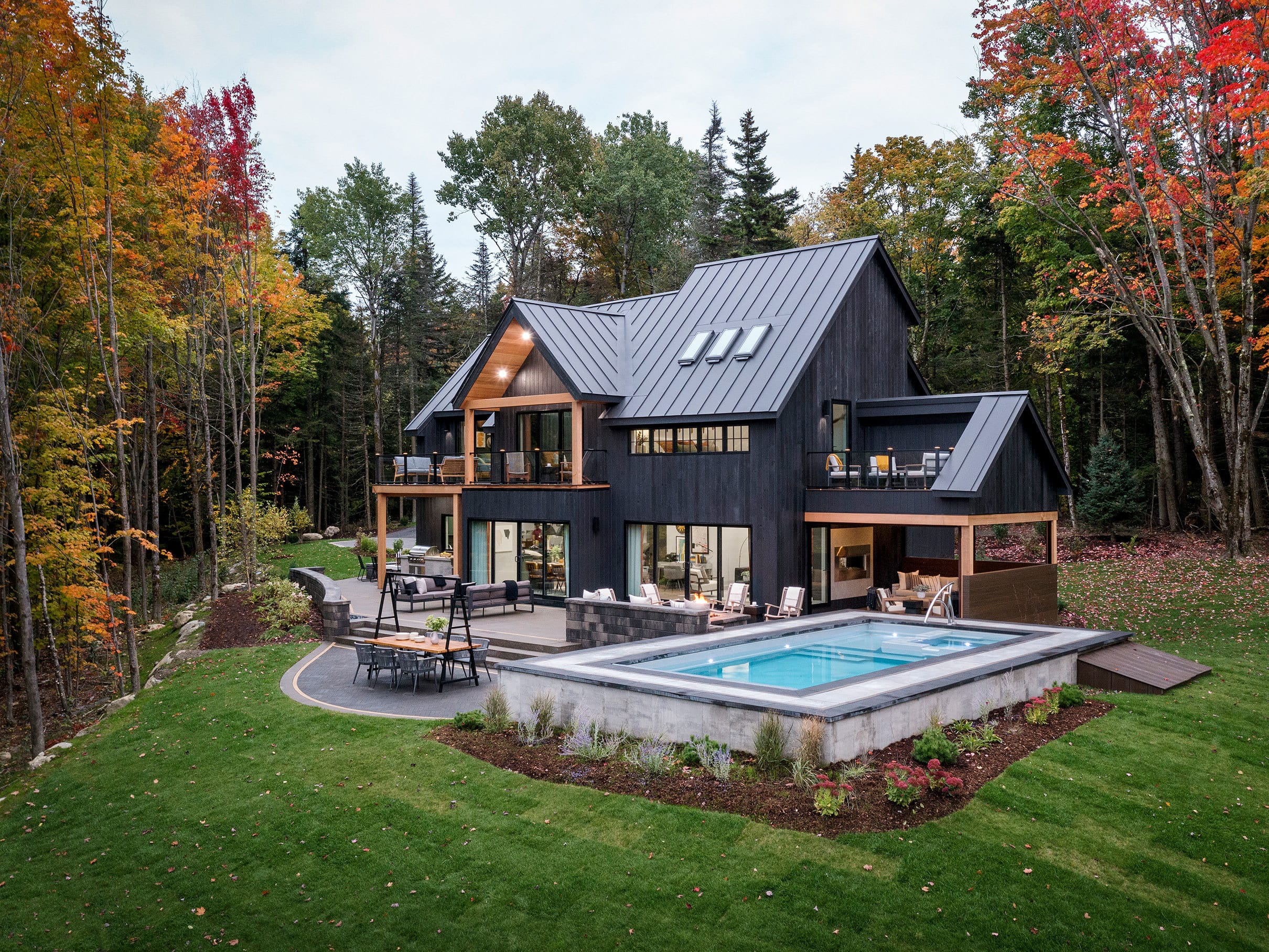 home exterior painted black with a metal roof and skylights surrounded by trees with autumn leaves