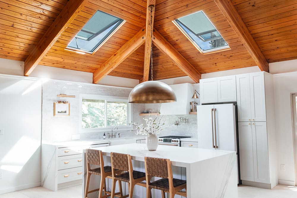 A white kitchen with a wood-clad ceiling that has two VELUX skylights installed.