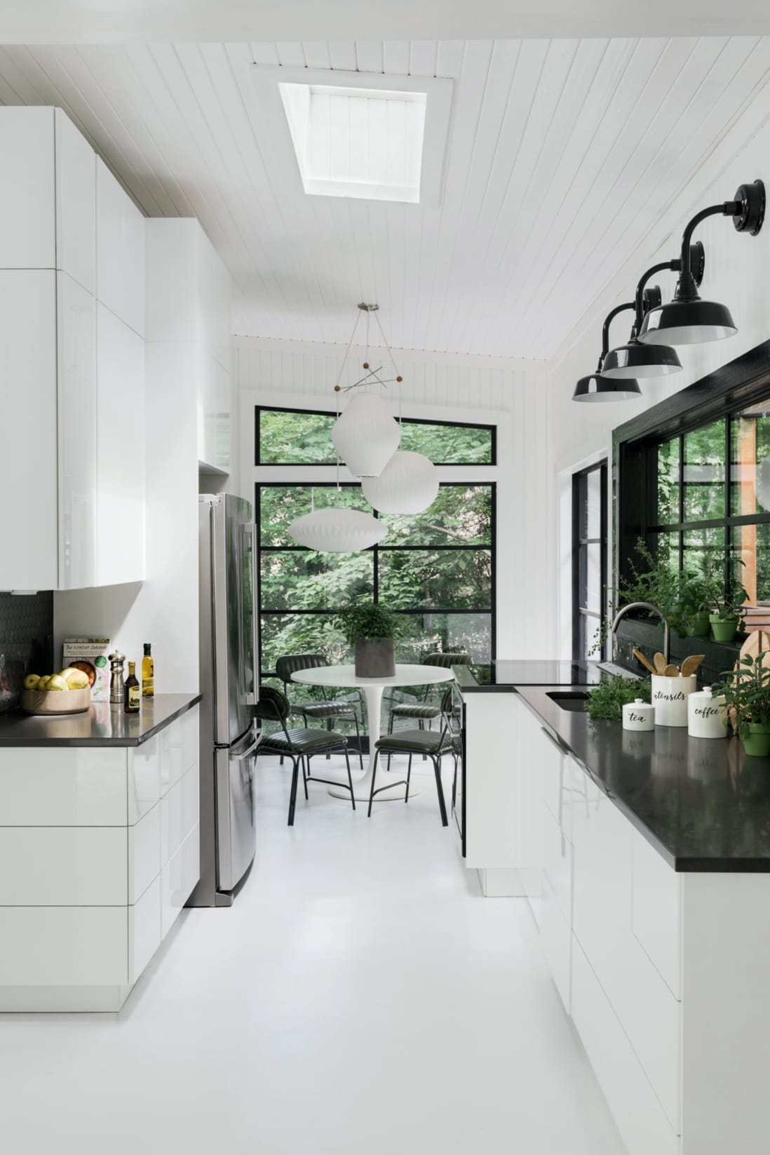 Skylight pours light into a narrow white kitchen with black countertops