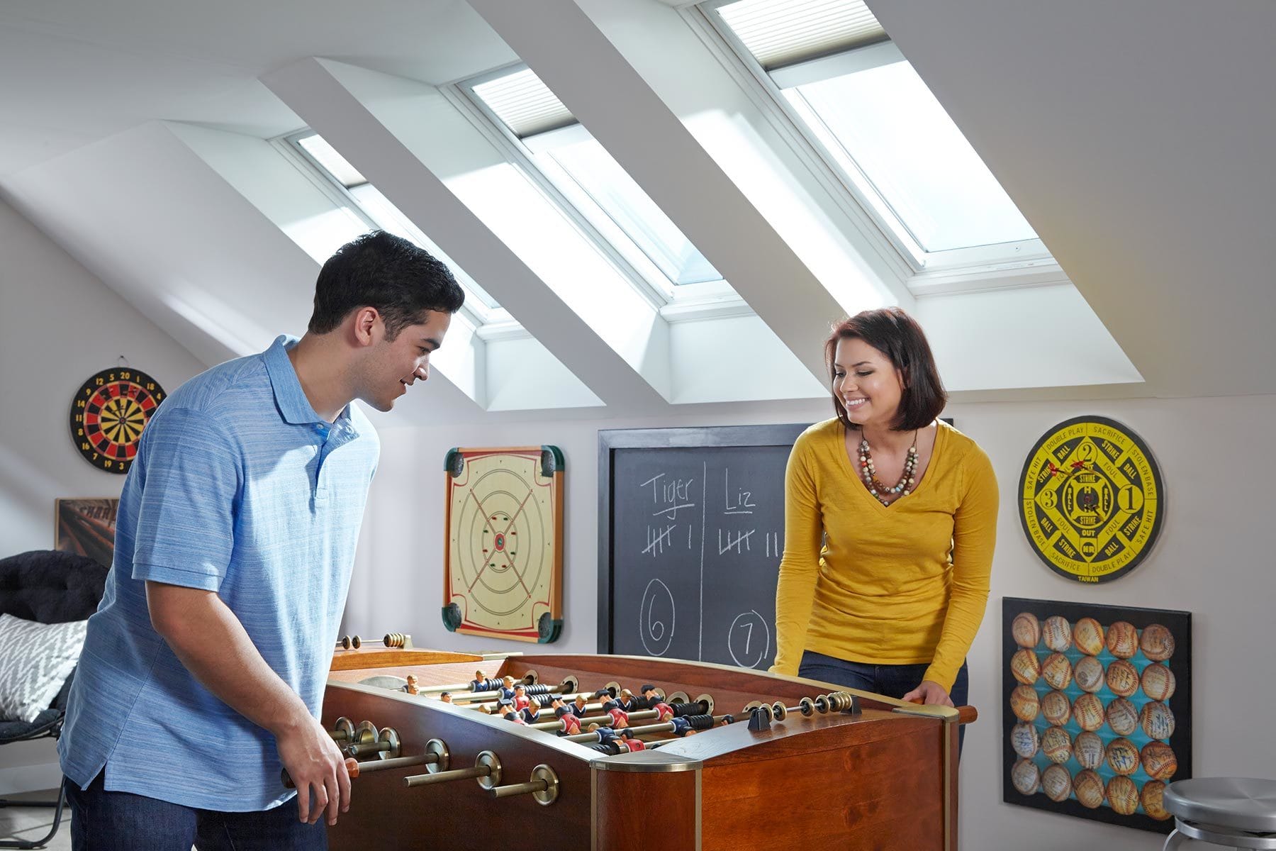 Close up of a man and woman playing on a foosball table in a bonus room under three skylights