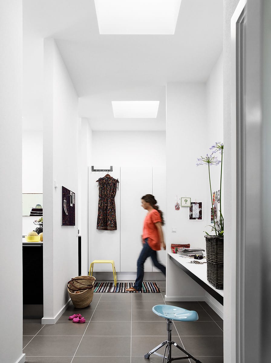 Woman walking in a bright white hallway with two skylights on the ceiling